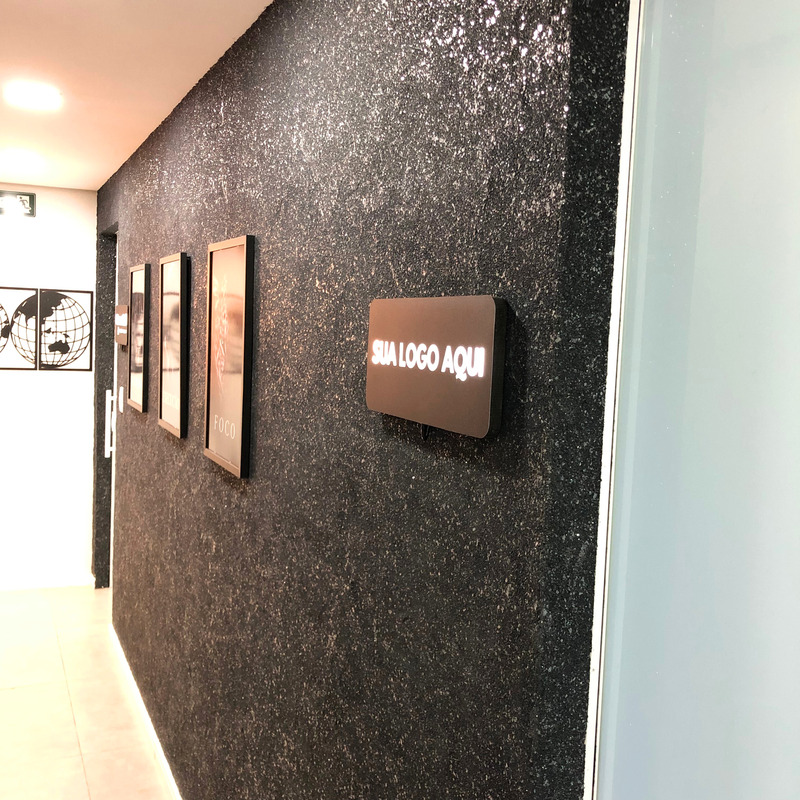 Na foto mostra a entrada de um escritório com a parede preta, com gliter e uma placa luminosa de led escrita "sua logo aqui".